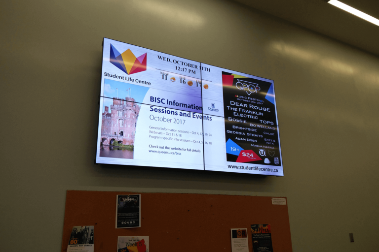 Student Life centre digital signage video wall displaying announcements, weather, and event information located above a bulletin board.