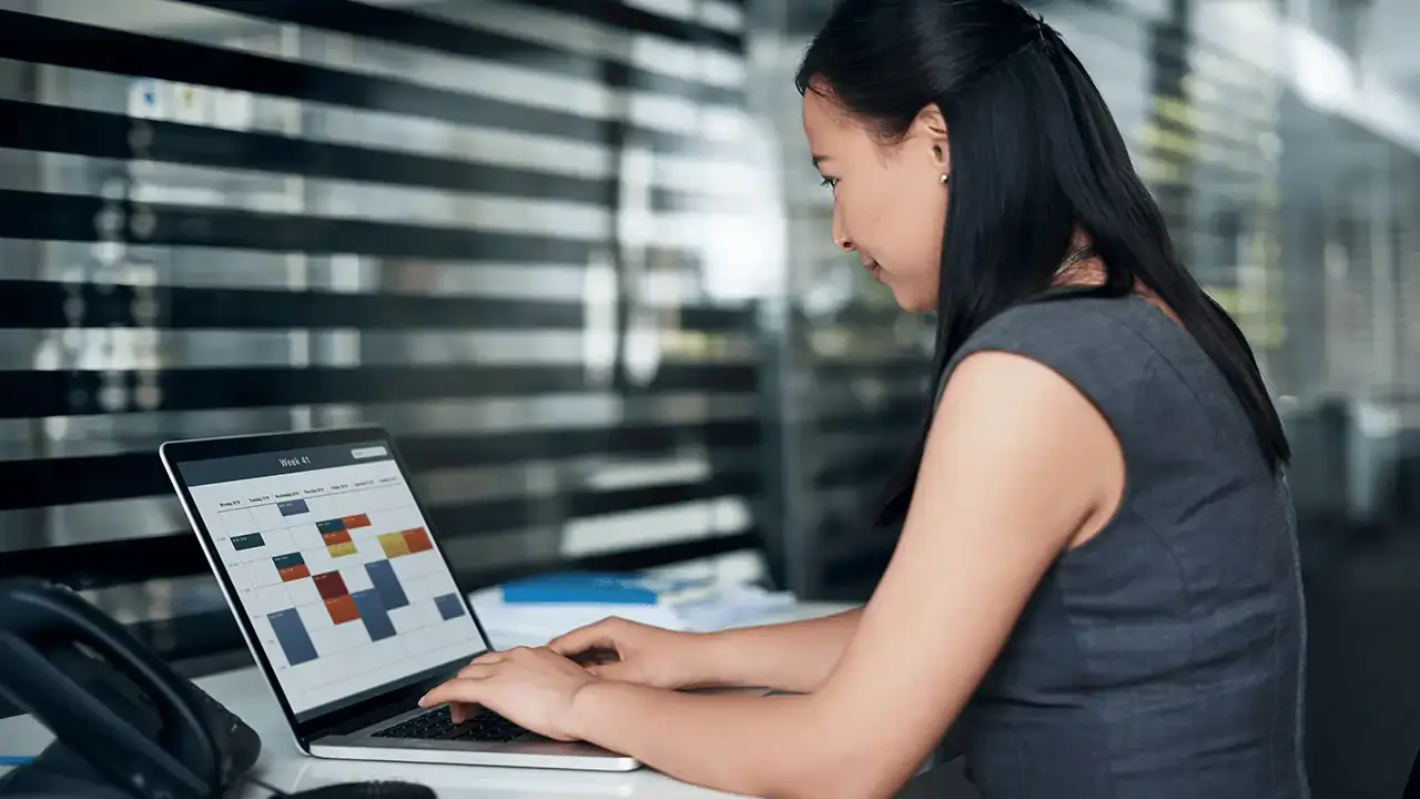 A woman seated with a laptop, making adjustments to their online calendar.