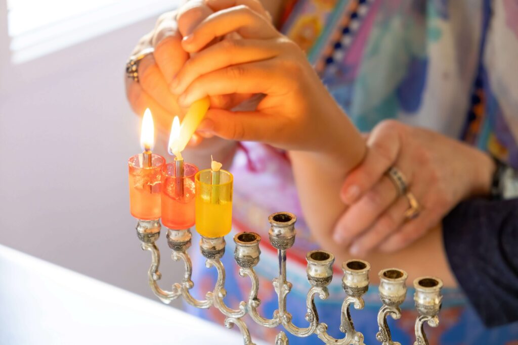Woman hands helping a child to light Hanukkah candle