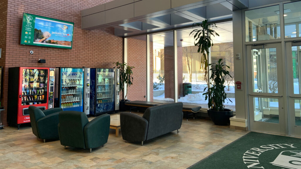 Colleges--Higher-Ed-min University lounge digital signage featured above snack and drink machines.