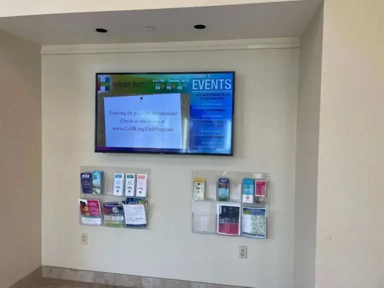 Hallandale Beach Parks & Rec digital signage from Reach Media Network featured above brochures and displaying events.