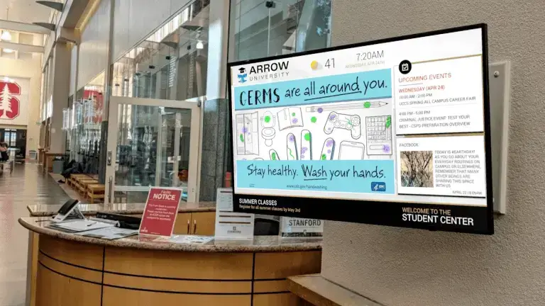 Arrow University digital signage screen from Reach Media Network featured at lobby front desk, displaying upcoming events, facebook post, and announcement about washing your hands.