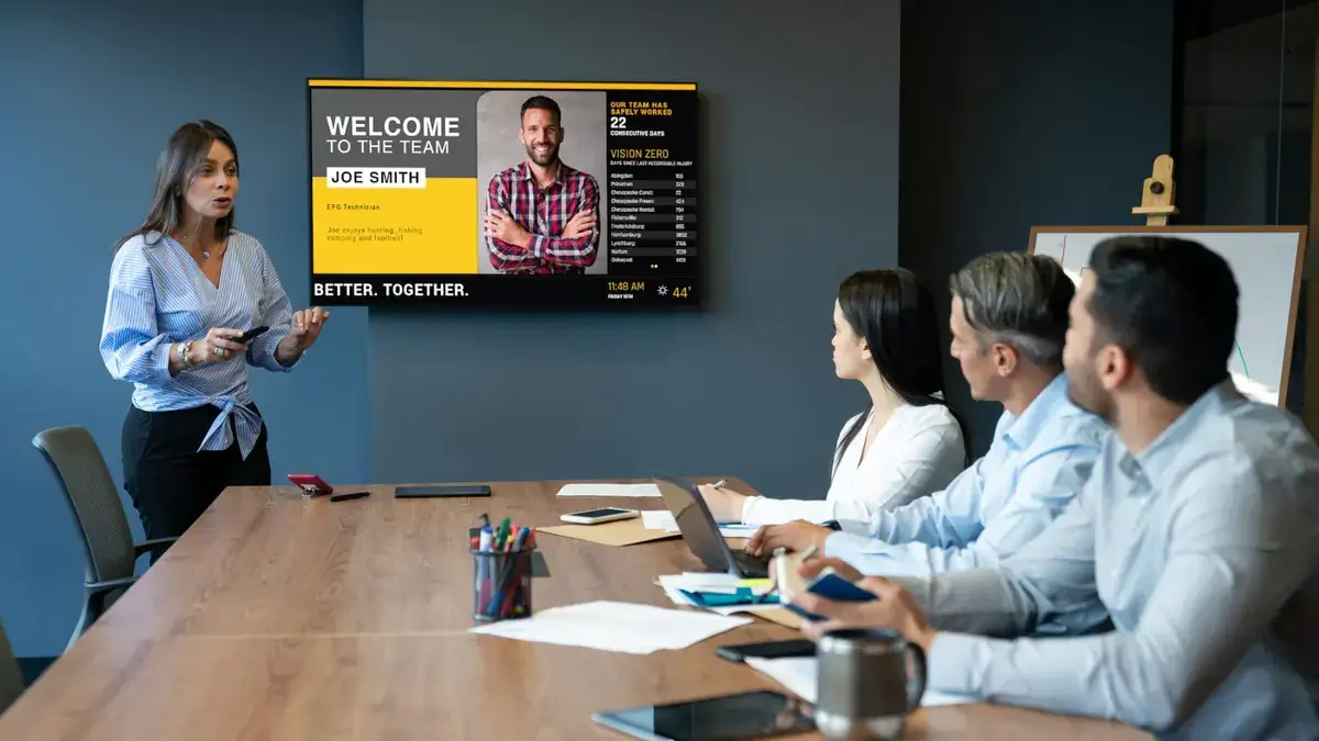 Board room digital signage from Reach Media Network displaying employee welcome message and business metrics.