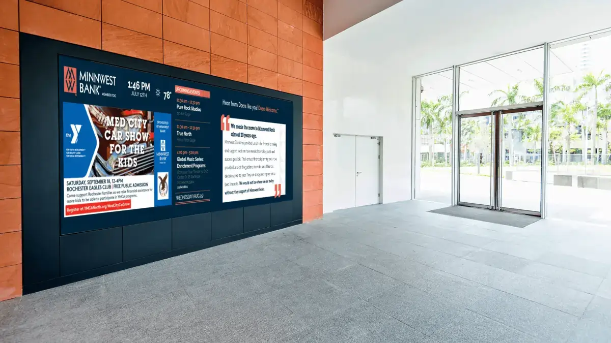Minnwest Bank digital signage screen from Reach Media Network featured at lobby entrance and displaying local YMCA announcement, customer reviews, and upcoming events.